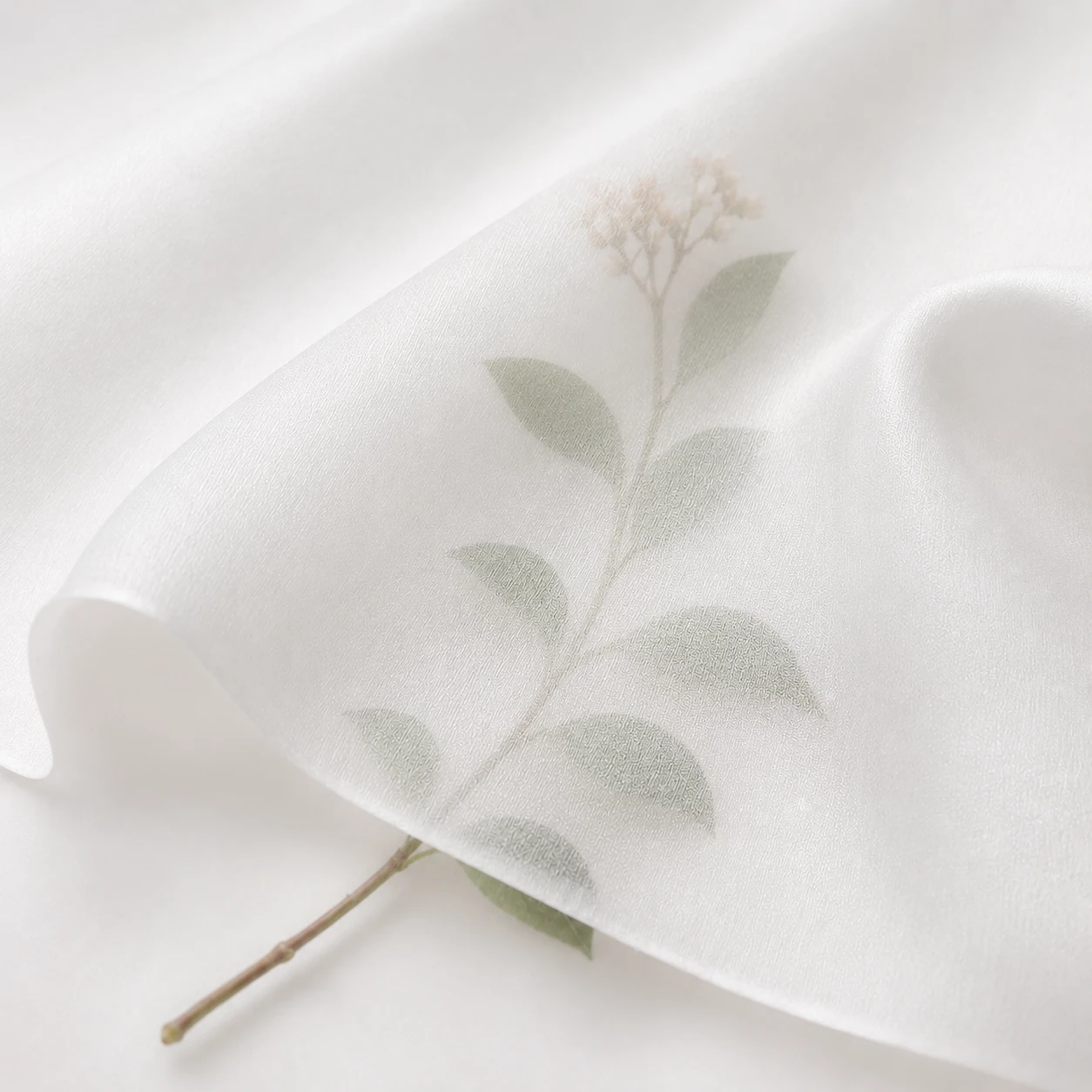Close-up of white silk twill fabric with soft transparency and a botanical stem visible beneath.