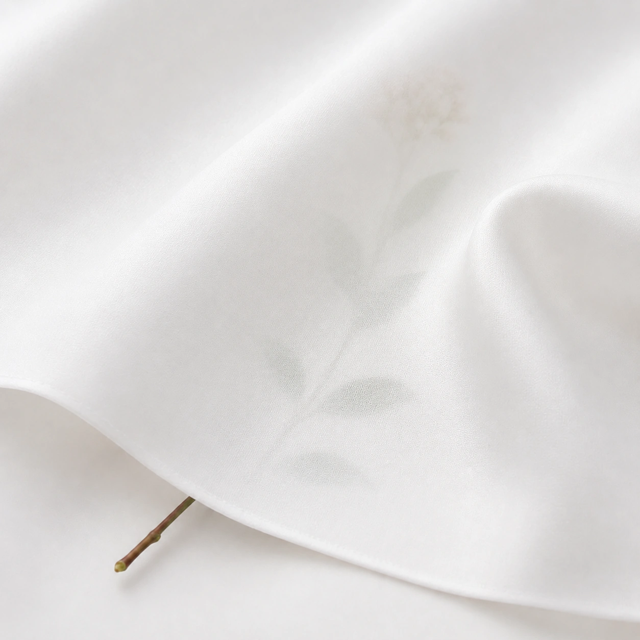White silk twill fabric with soft transparency and a faint botanical silhouette visible underneath.